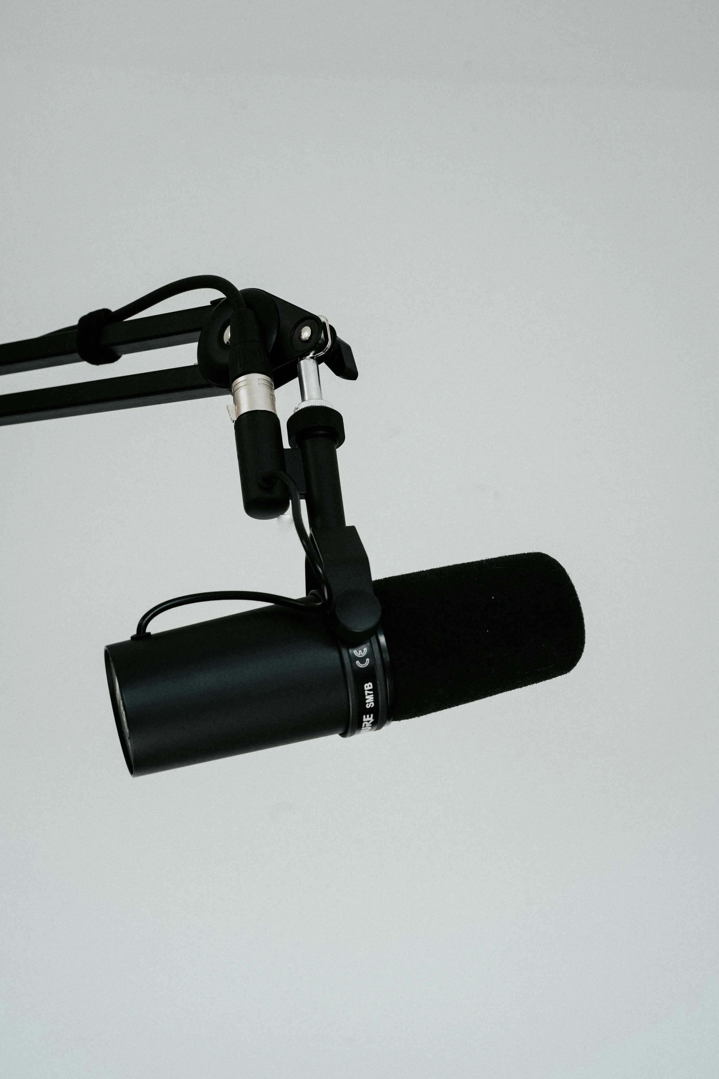 Close-up of a professional black microphone with a foam windscreen, mounted on a stand against a plain white background.