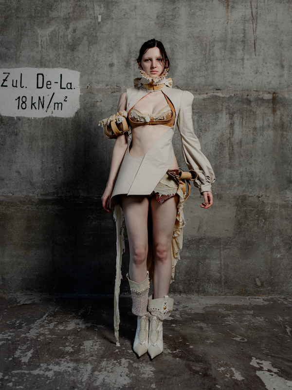 Lookbook-Chrysalis-janiejeanEine junge Frau in einer avantgardistischen, unkonventionellen Mode zeigt sich vor einer rohen Betonwand.