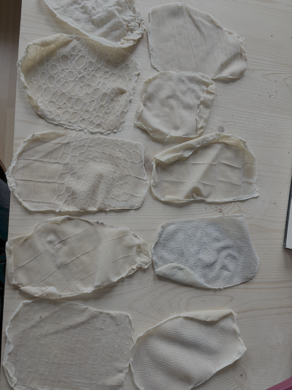 janiejean-Latex-Textile-surfaces, Verschiedene weiße Textilien mit unterschiedlichen Mustern und Texturen auf einem weißen Tisch ausgebreitet.