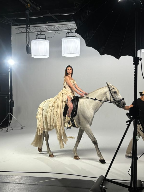 Frau in einem Vintage-Kleid reitet auf einem weißen Pferd in einem professionellen Fotostudio mit Fotolicht und Hintergrund.