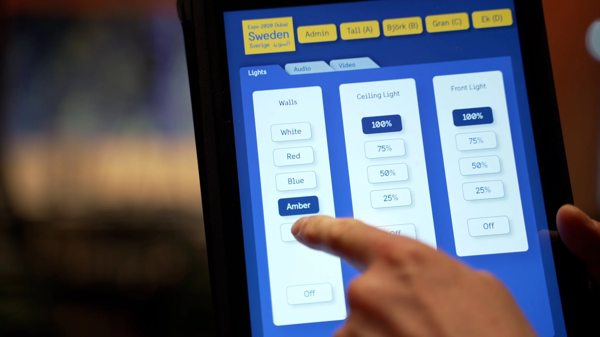 A person interacts with a touchscreen light control panel showing different lighting options for walls, ceiling light, and front light, with adjustable brightness percentages.