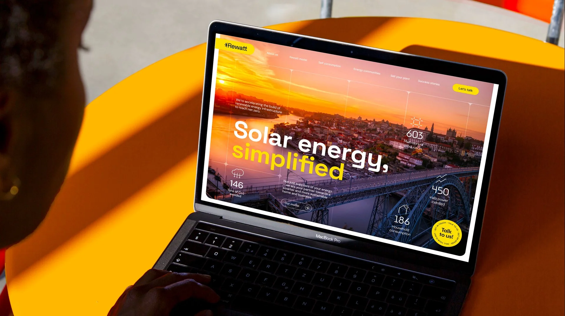 A person using a MacBook Pro laptop to view a website about solar energy, with a sunset over a cityscape in the background, featuring charts and statistics related to renewable energy.