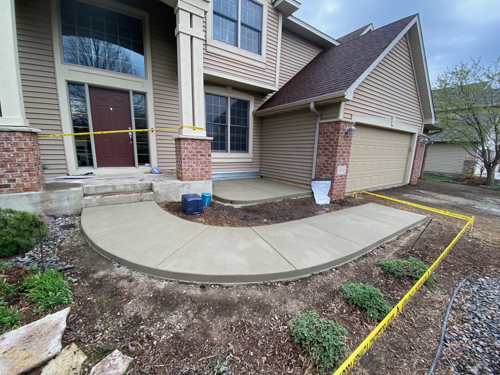 New concrete walkway leading to front door and garage of a house under construction, with yellow caution tape surrounding the work area.