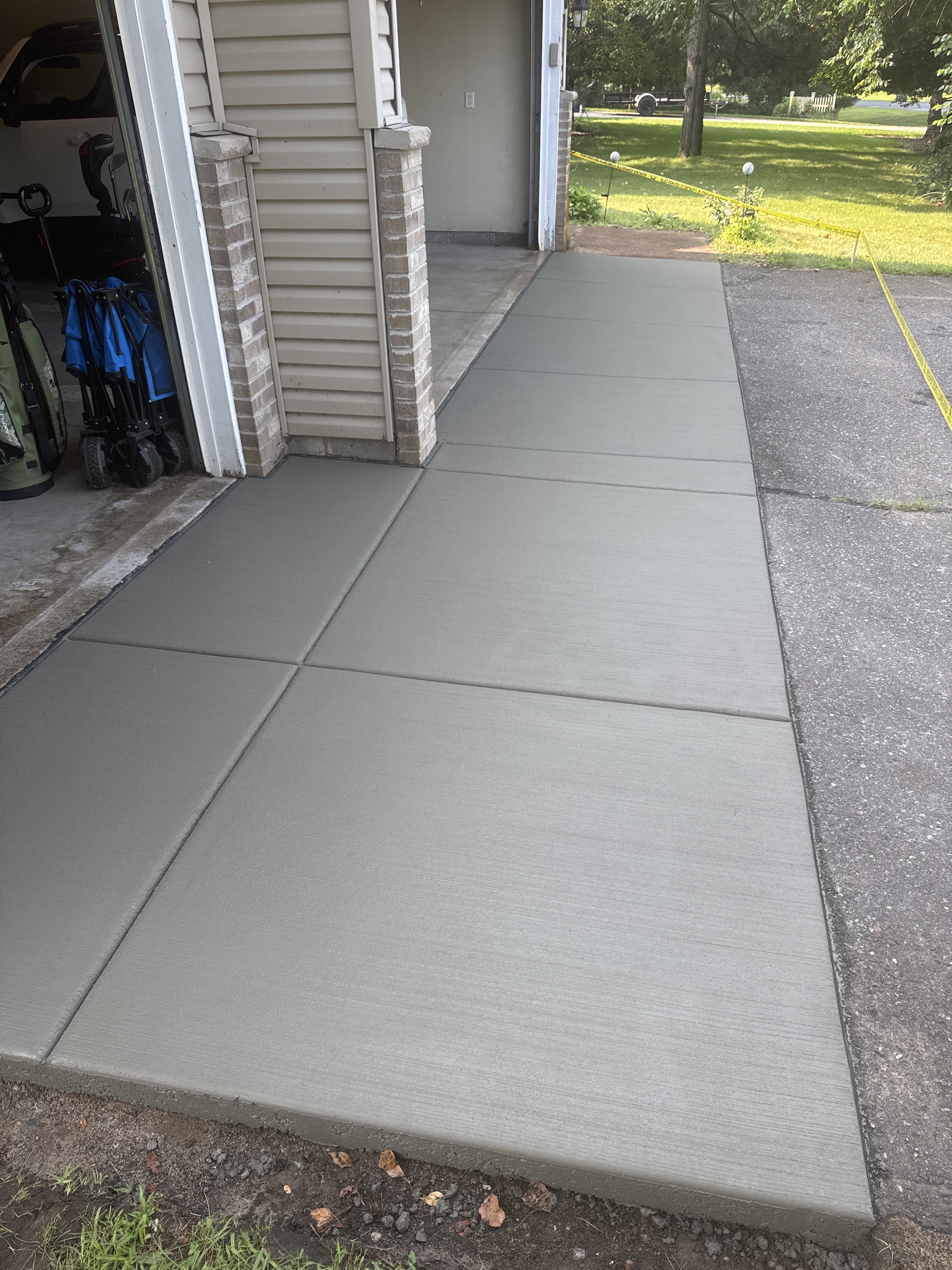 Freshly poured concrete sidewalk leading from garage to driveway outside a house.