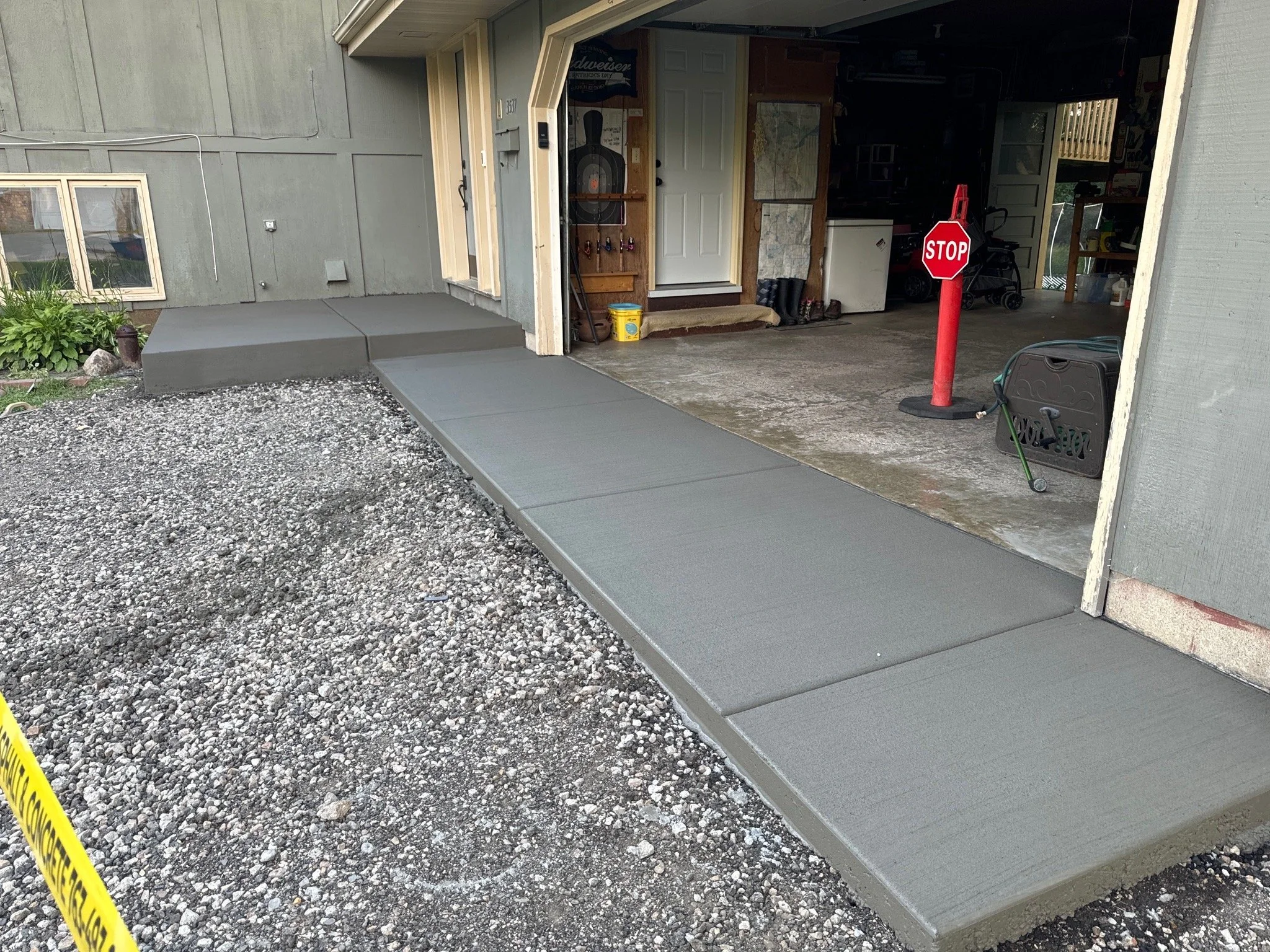 Concrete parking curb being installed in a garage entrance with a new concrete sidewalk outside, and a stop sign placed on a red stand inside the garage.