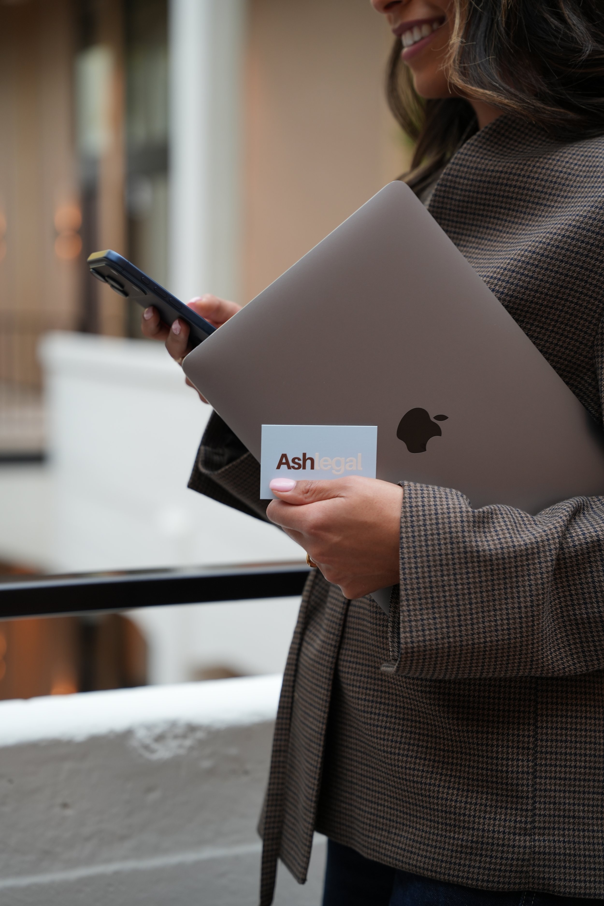 Close-up van een vrouw die een smartphone vasthoudt, een laptop en een visitekaartje met de tekst 'Ash Legal'.