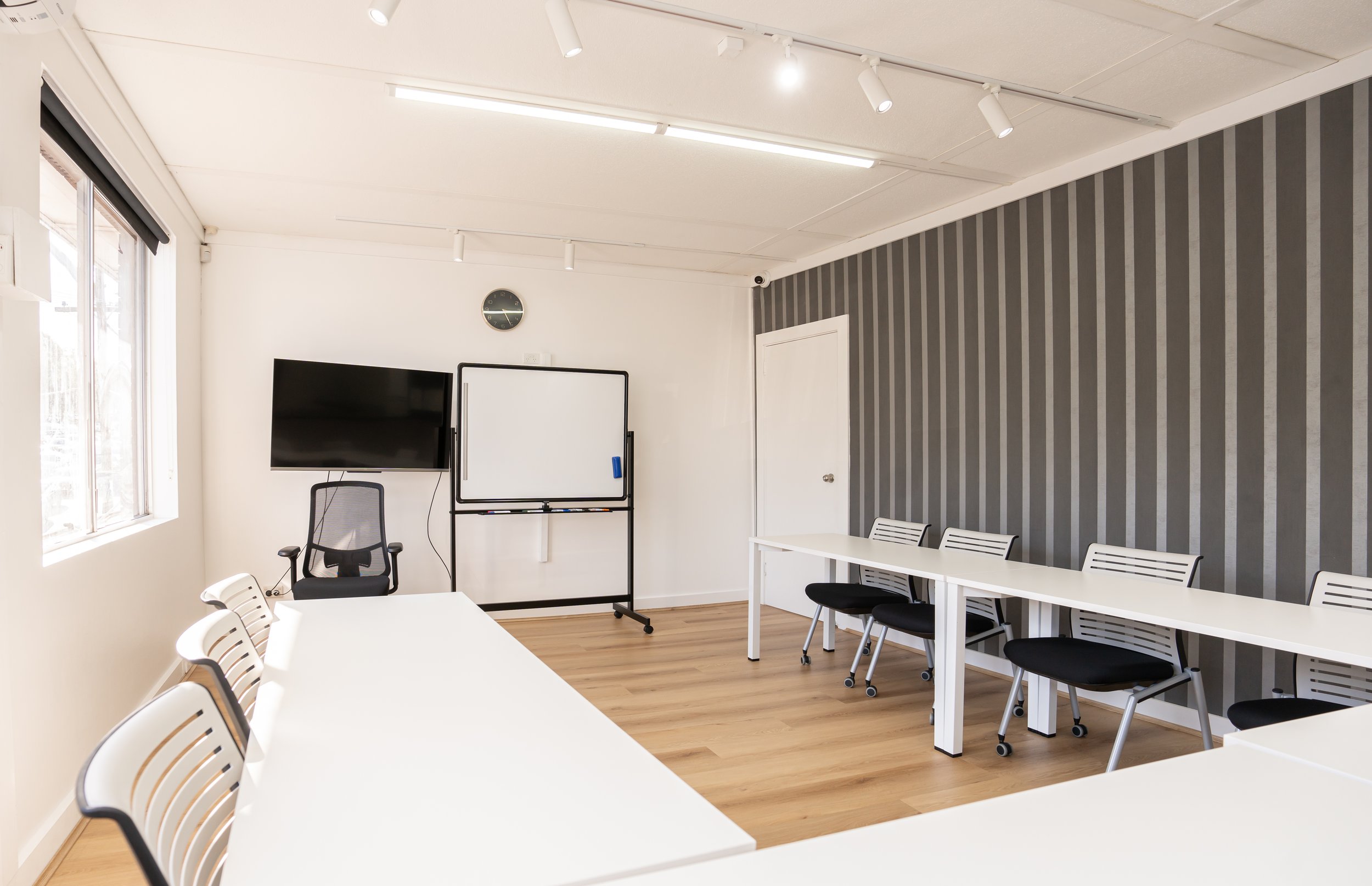 Empty modern meeting room with white tables, black chairs, a whiteboard, a TV, and a striped accent wall.
