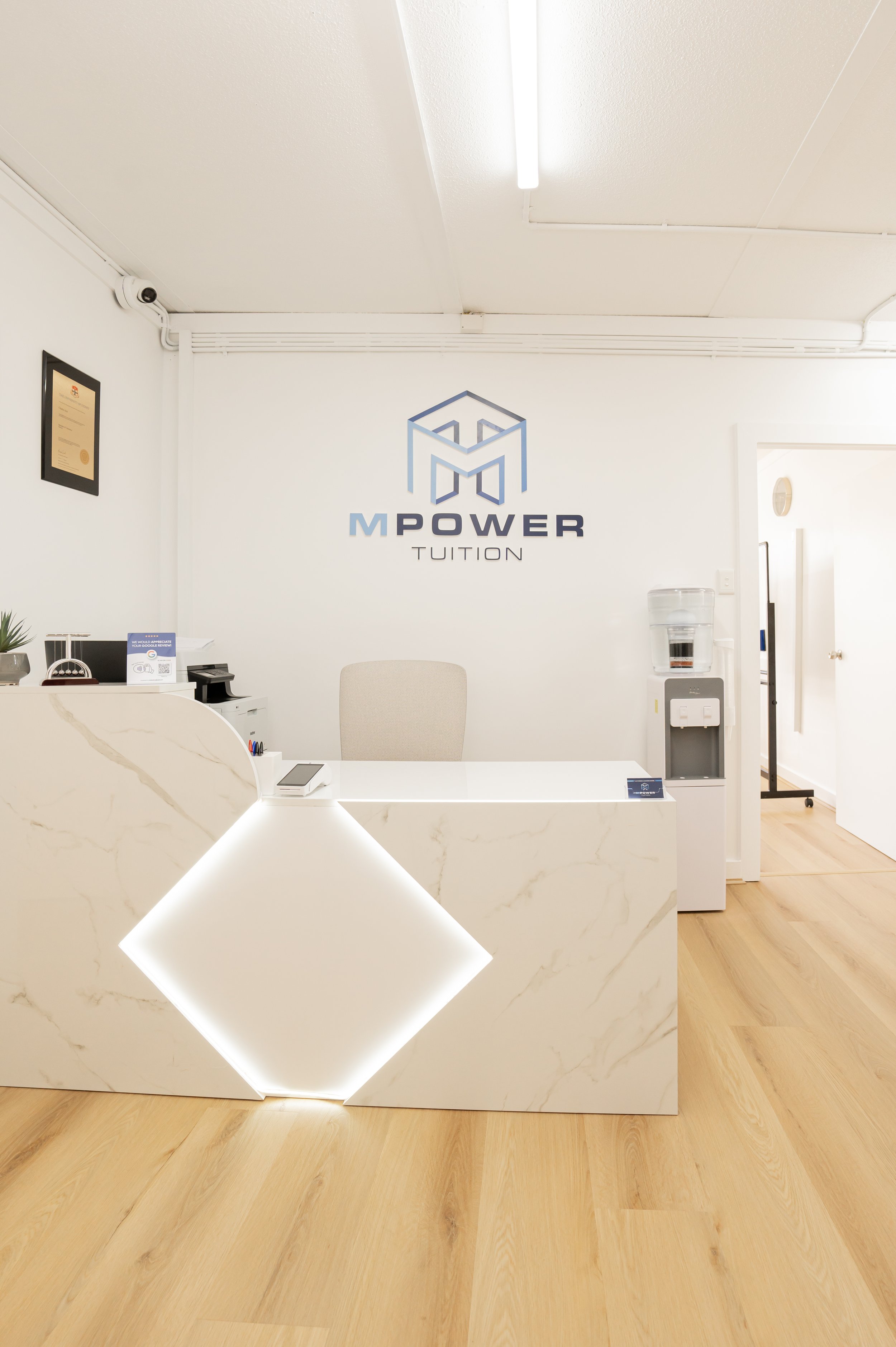 Reception desk in an office with a logo on the wall that says 'M Power Tuition' and a water dispenser beside the door.