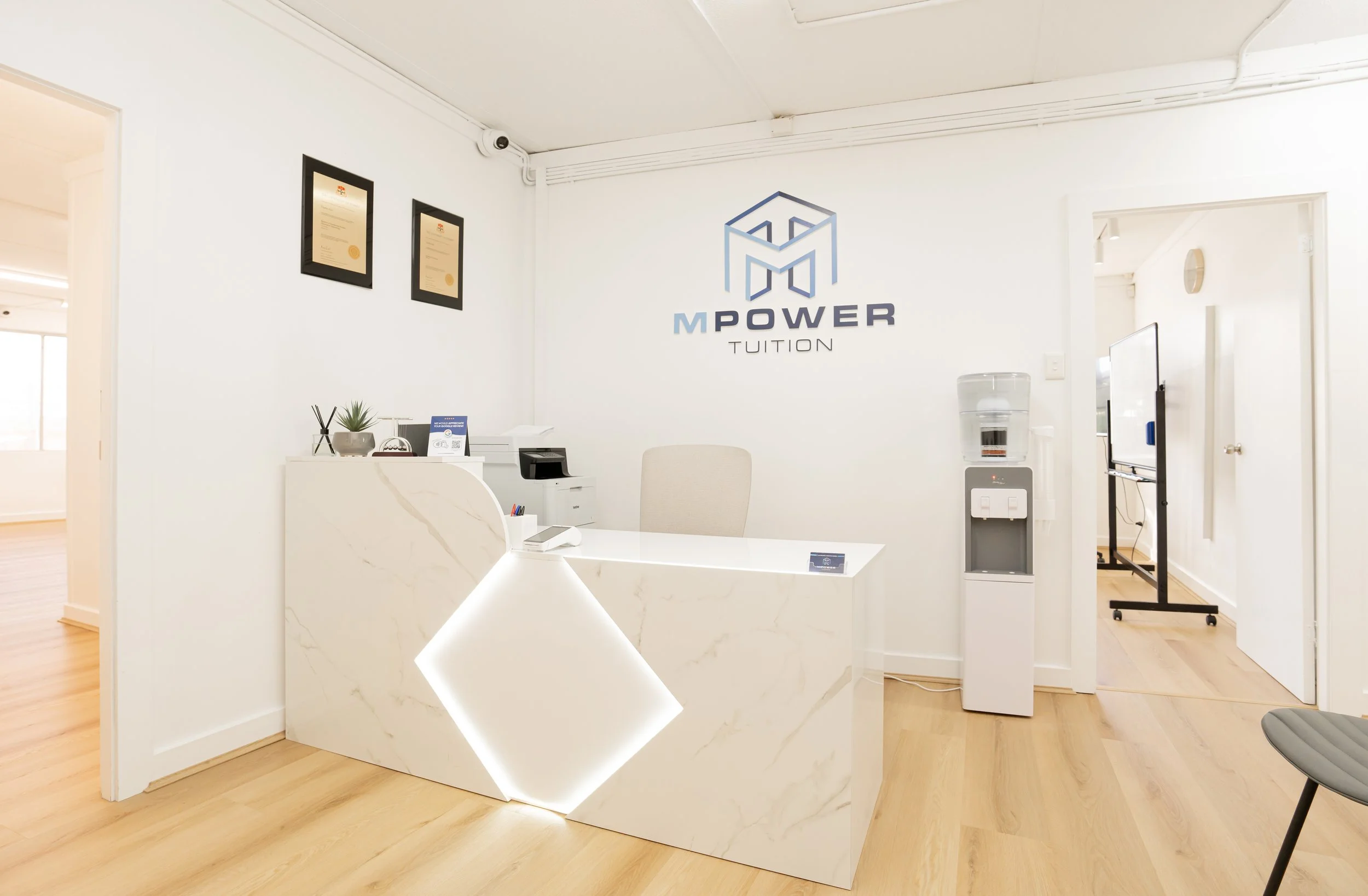 Modern reception area with white marble desk, water cooler, wall art, and a logo on white wall.
