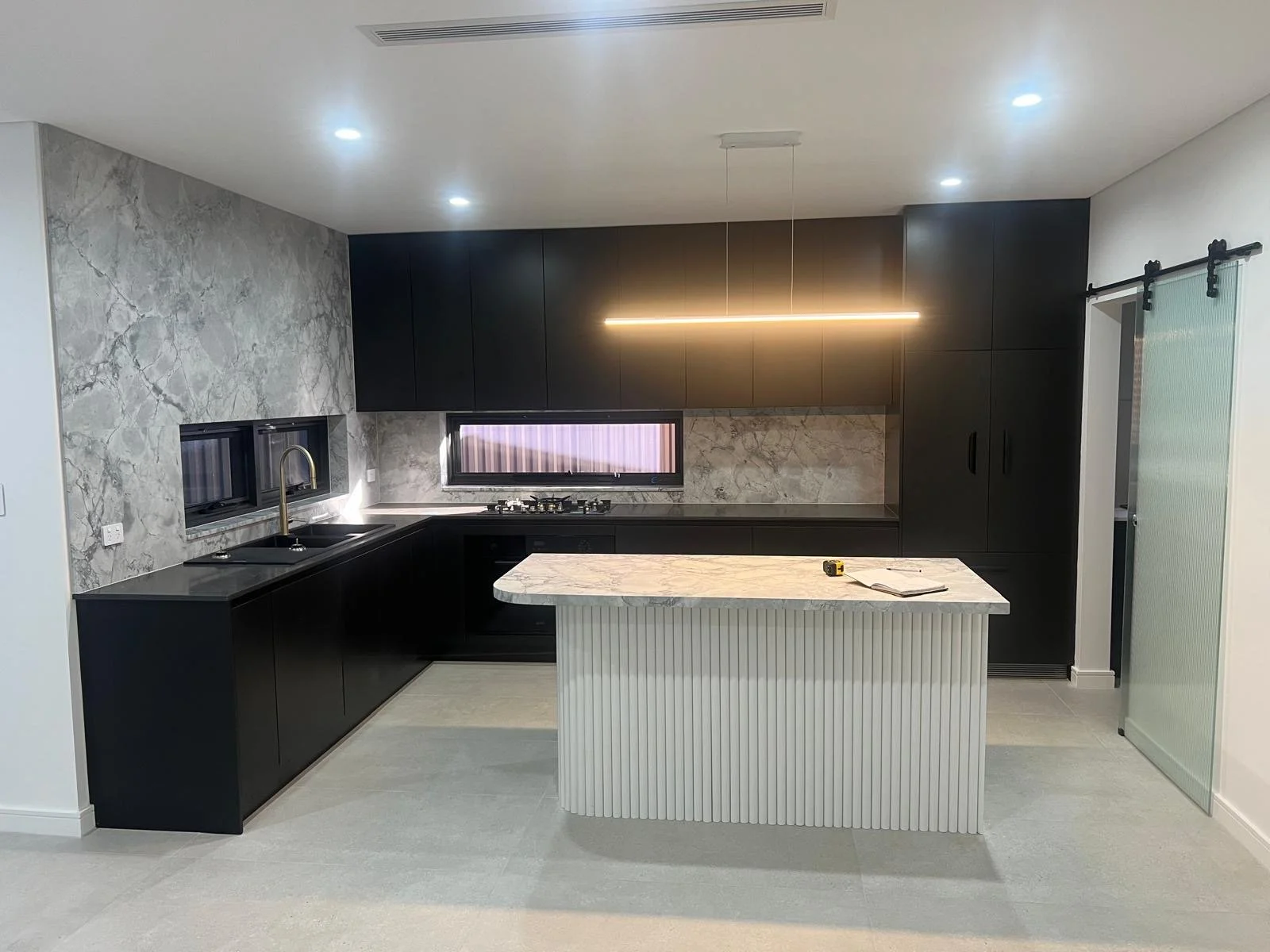 Modern kitchen with black cabinetry, marble backsplash, island with marble top, and sliding glass door.