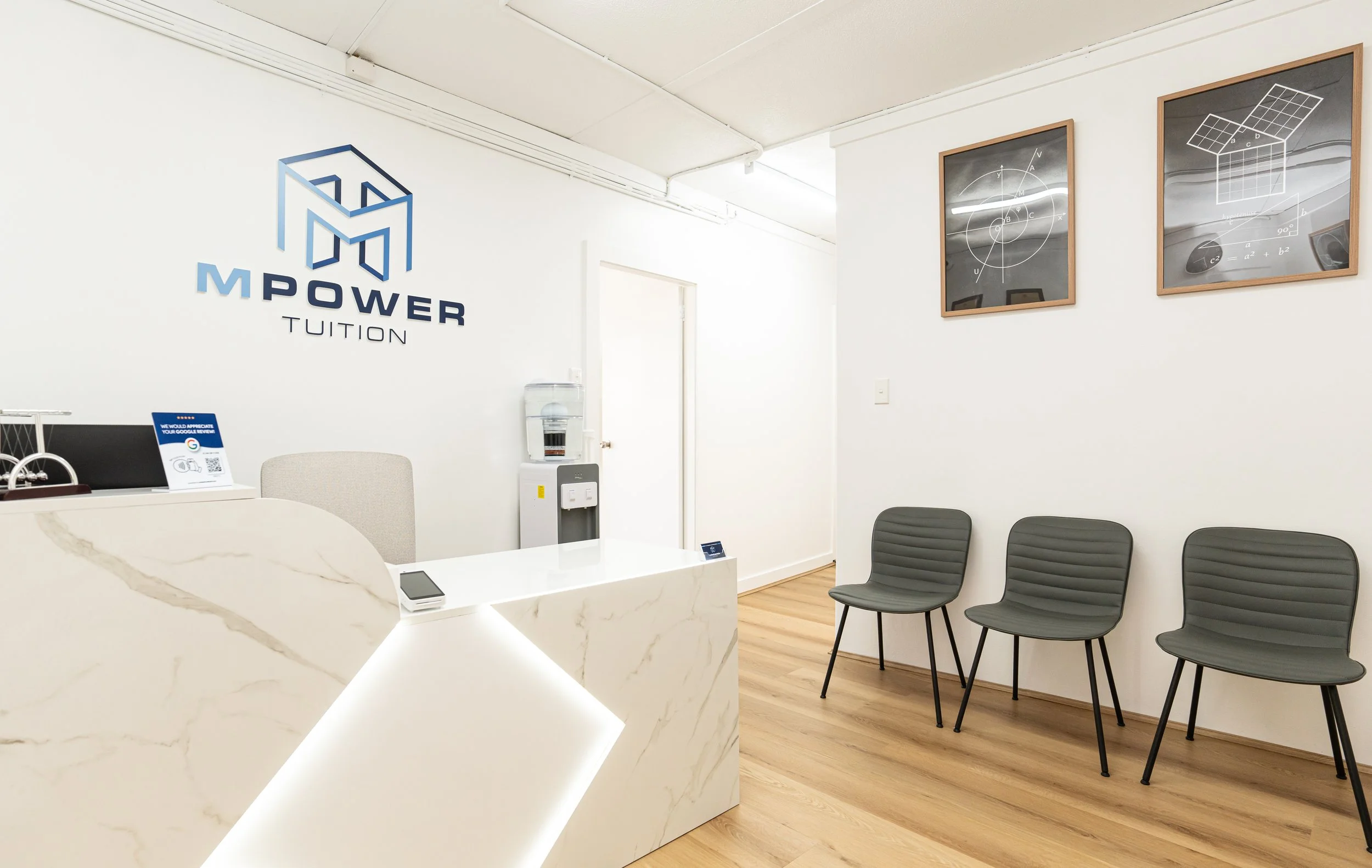 Reception area with a marble desk, three gray chairs, a water dispenser, and framed geometric diagrams on the wall.