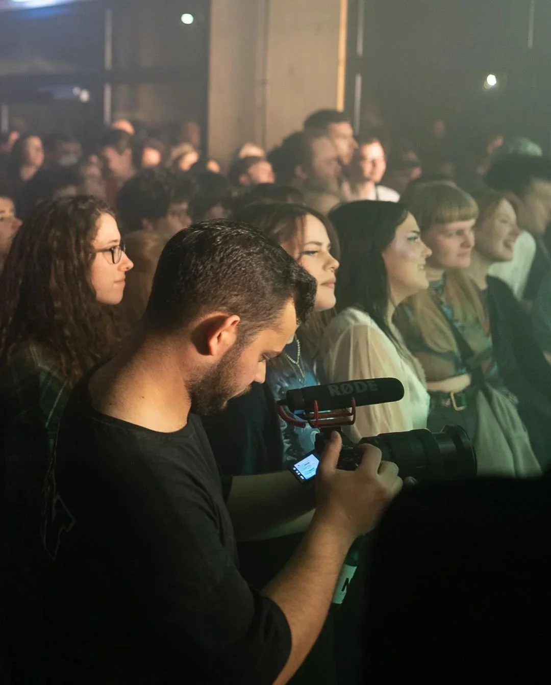 Ein Fotograf mit einer Kamera und einem Rode Mikrofon vor einer Menschenmenge bei einem Event.