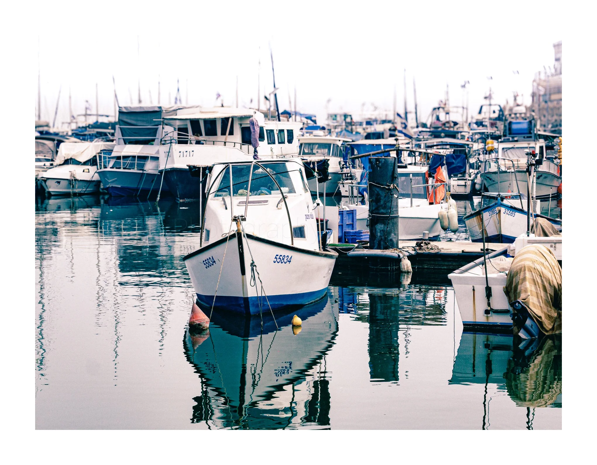 Various boats and yachts docked at a marina with their reflections in the calm water.
