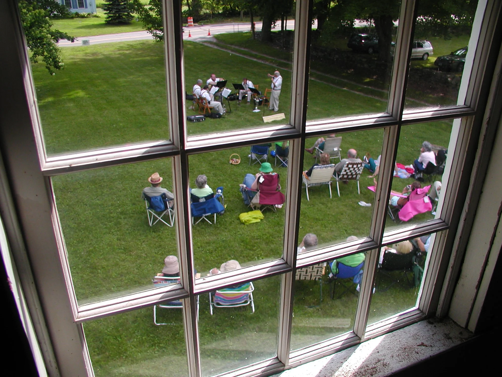 An overview showing a small outdoor concert with Quintebrass performing on the grass and an audience sitting on chairs and blankets.