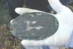 Person wearing a white glove holding an elongated, dark-colored artifact or stone with worn, chipped edges.