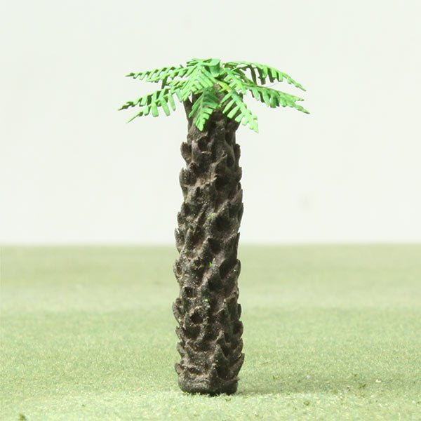 Plastic model palm tree with green leaves and textured brown trunk on green surface.
