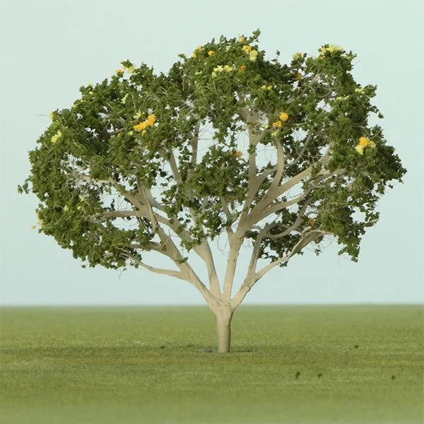 A model tree with a white trunk and green foliage with yellow flowers, standing on a grassy field against a clear sky.