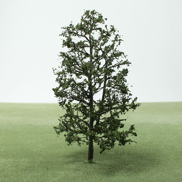 A solitary model tree with green leaves stands on a grassy field against a plain, light-colored background.