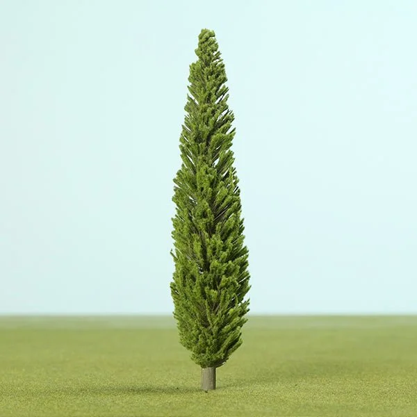 A tall, narrow model evergreen tree planted in the ground on a grassy surface with a pale sky background.