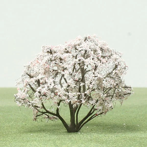 Small blooming model cherry blossom tree with pink and white flowers on a grassy surface.