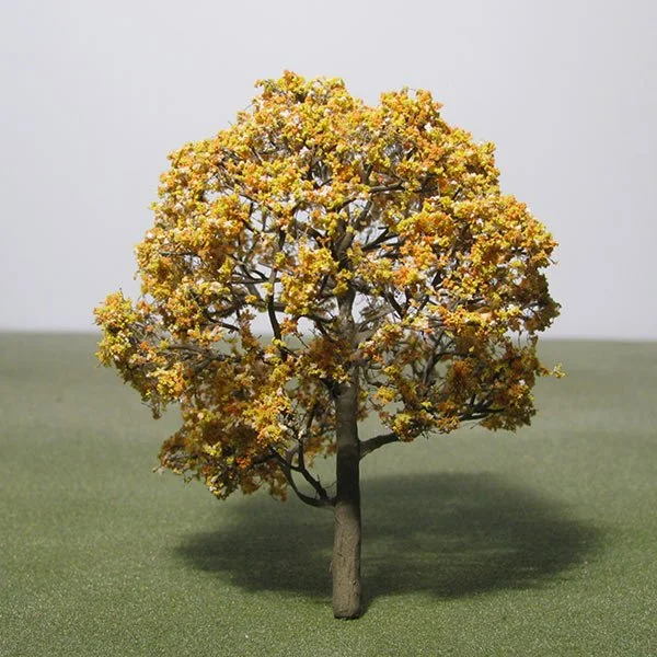 Model of a tree with yellow and orange leaves, positioned on a green surface with a plain background.