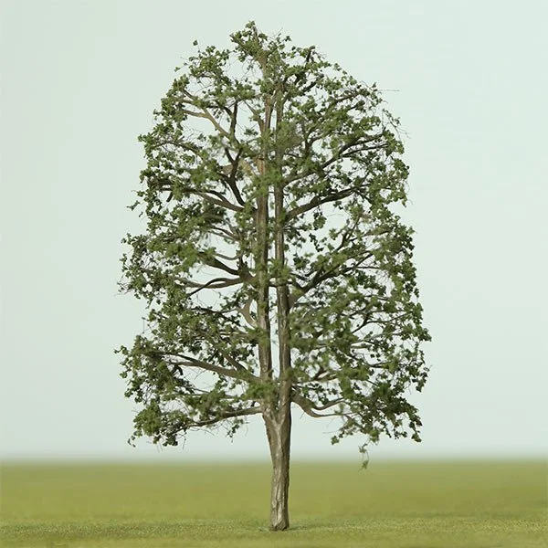 A tall model tree with sparse green leaves standing alone on a grassy field.