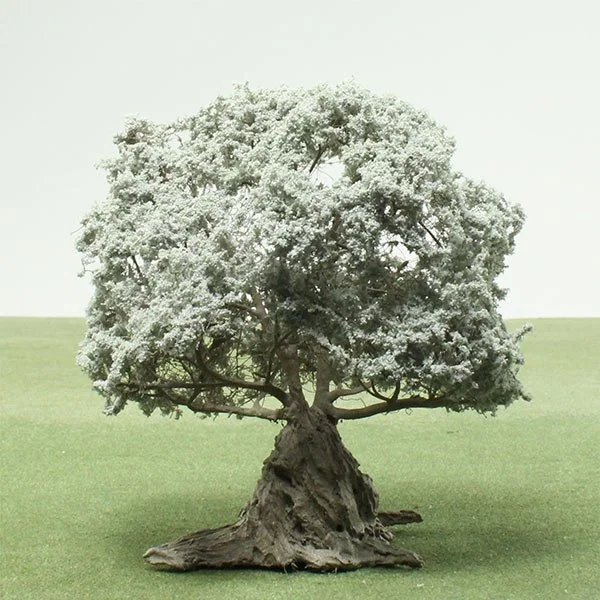 A model bonsai tree with a thick, gnarled trunk and full, rounded canopy of small leaves, set on a flat grassy surface.
