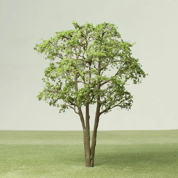 A single green model tree with multiple branches stands in the middle of a grassy field against a plain, light-colored sky.