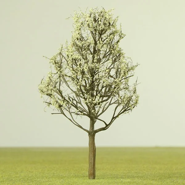 A solitary model tree with light-colored blossoms standing on a grassy field against a plain light background.