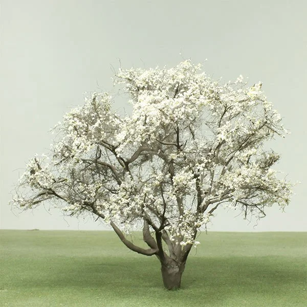 A model tree with white blossoms standing in a grassy field against a light sky.