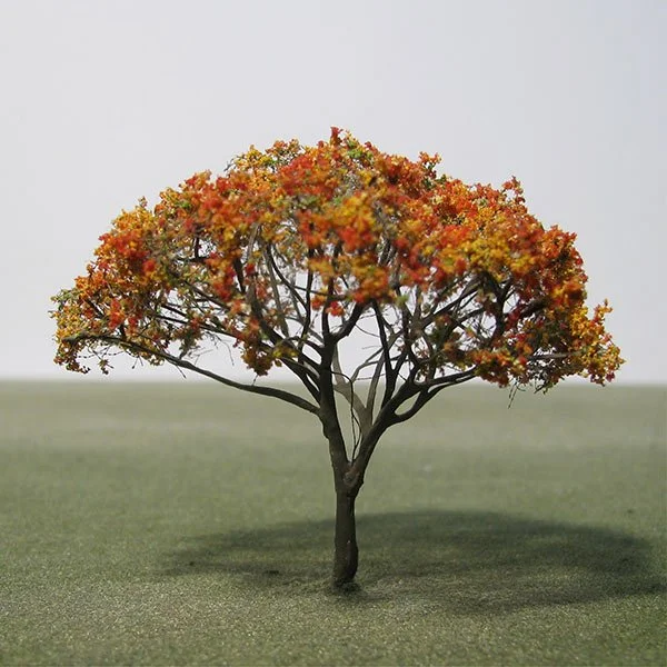 A small model tree with orange and yellow leaves on a patch of grass.