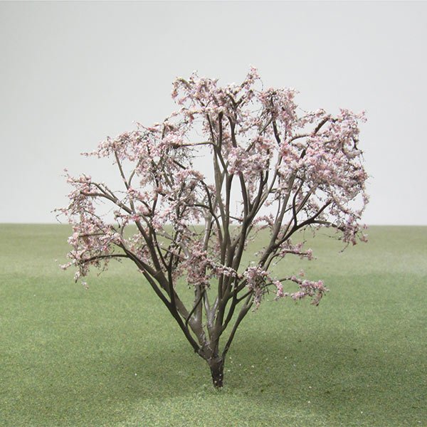 A small model tree with pink flowering blooms, set against a plain background with green ground.