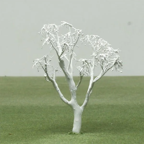 A small, bare model tree painted white, standing on a grassy field.