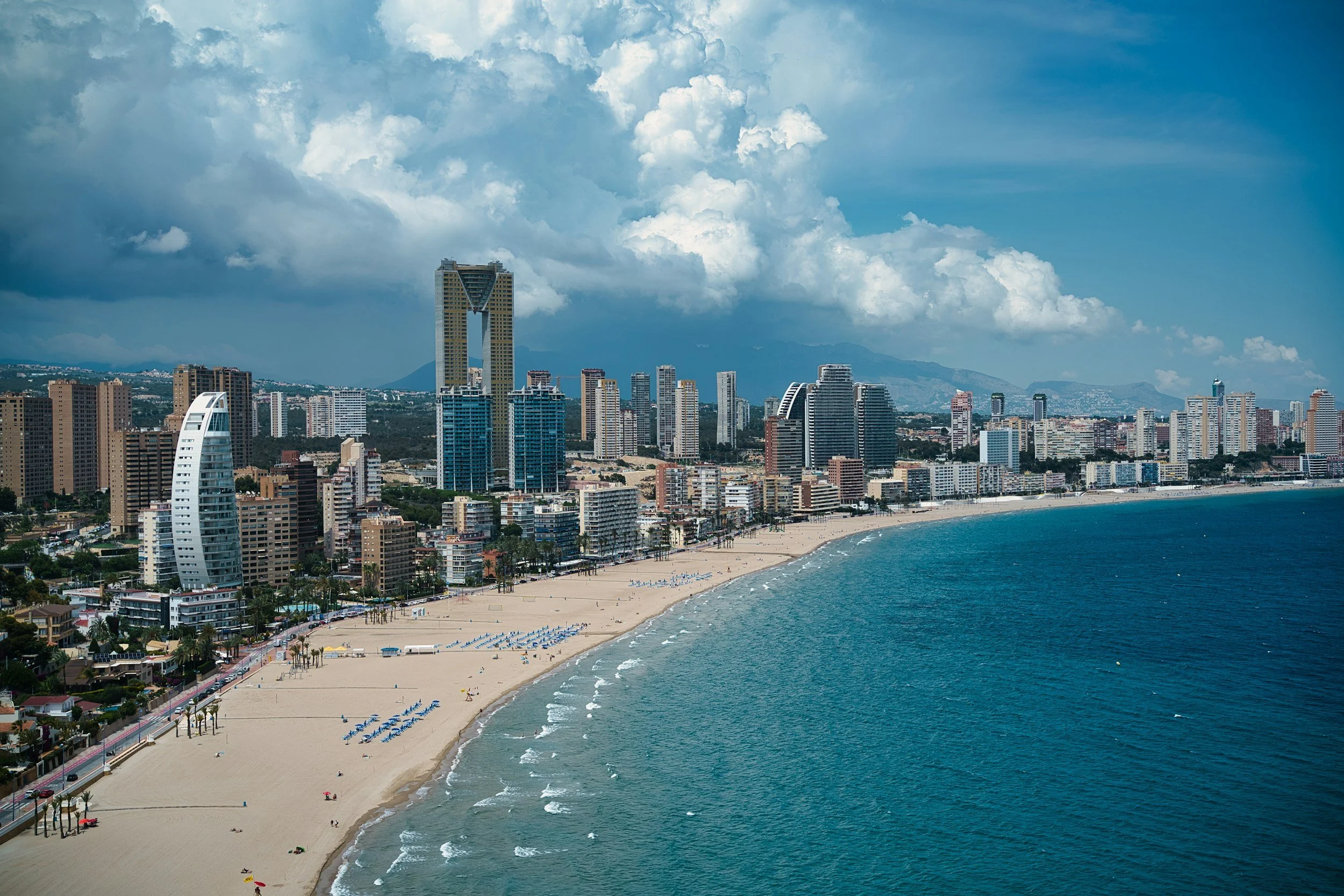 Vista aérea de la playa y el skyline de la ciudad con edificios altos frente al mar bajo un cielo nublado.