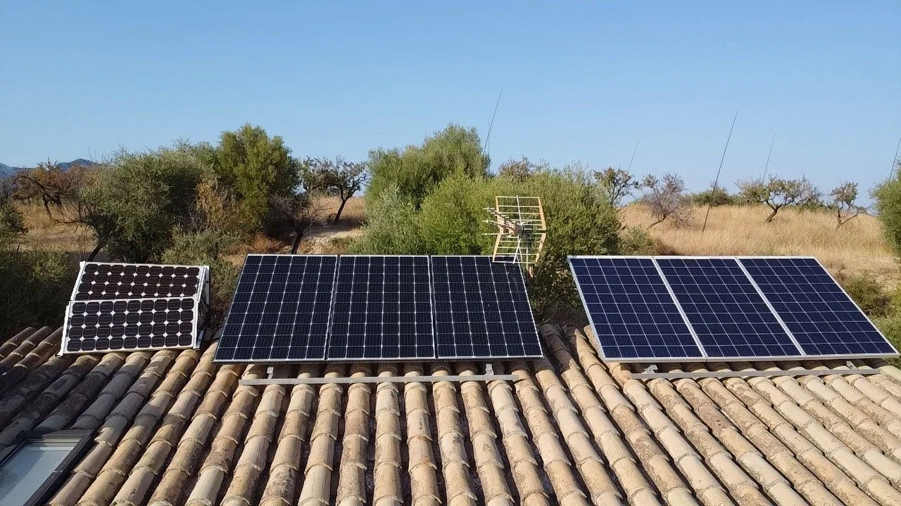Three solar panels installed on a tiled roof with trees and a clear blue sky in the background.