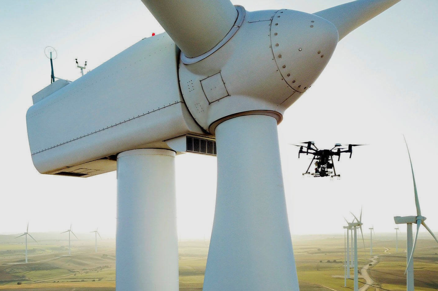 A drone flying near a large wind turbine in a wind farm.