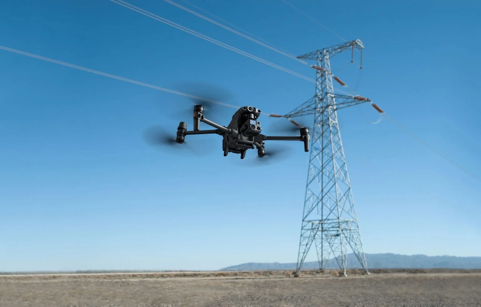 A drone flying near an electrical transmission tower against a clear blue sky.