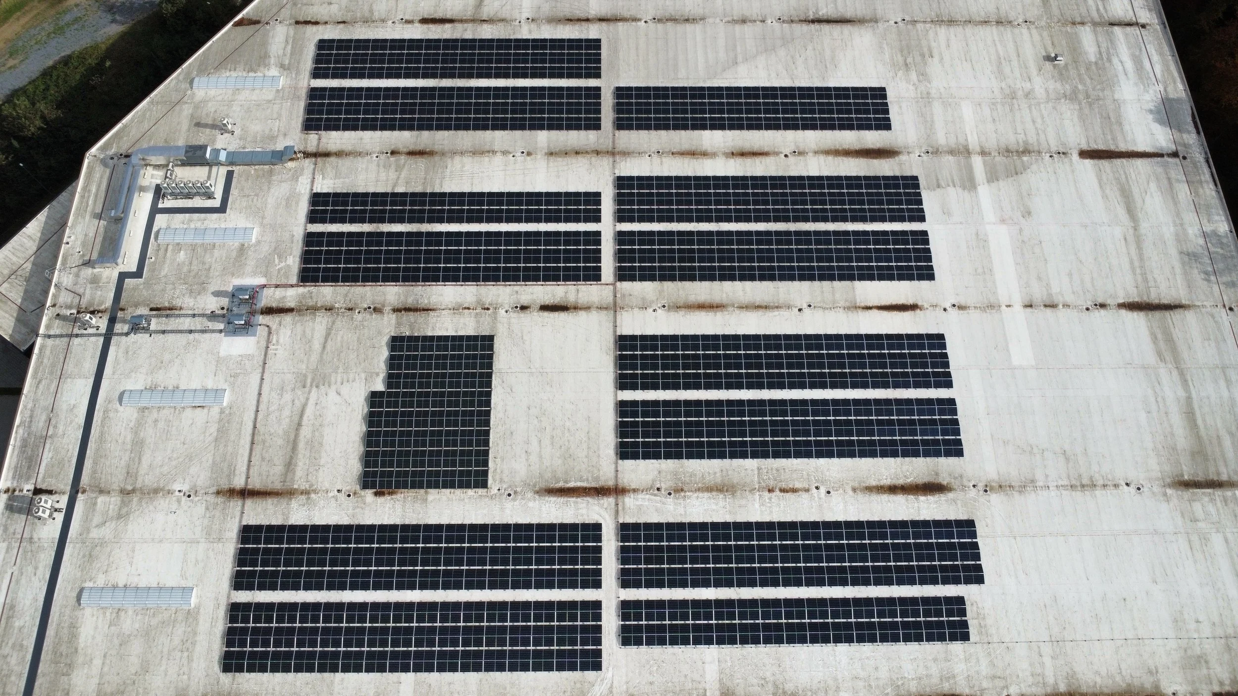 Aerial view of a large white industrial building roof with multiple solar panels installed.