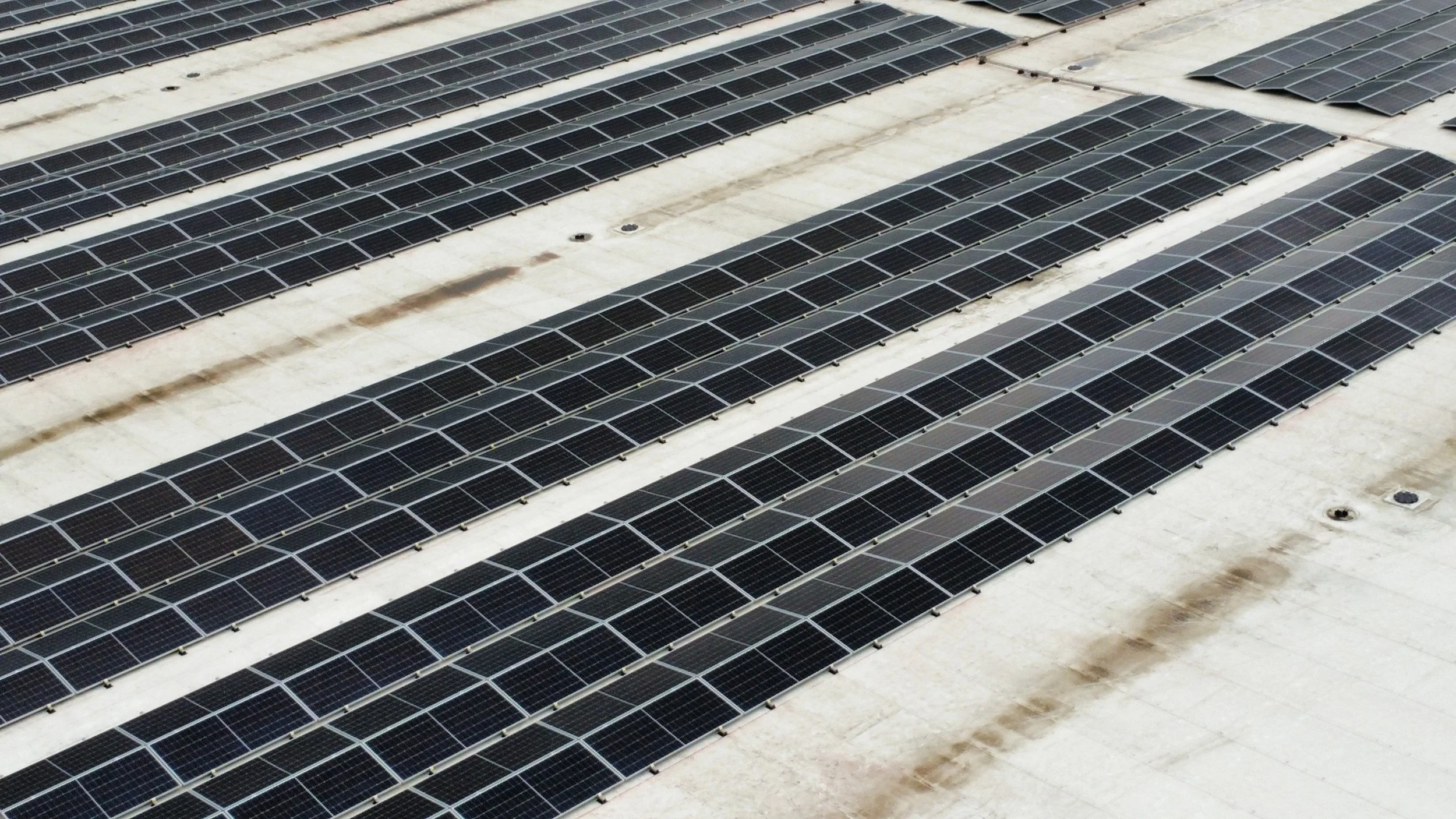 Multiple rows of solar panels installed on a flat rooftop, with some dirt and stains visible on the white surface.