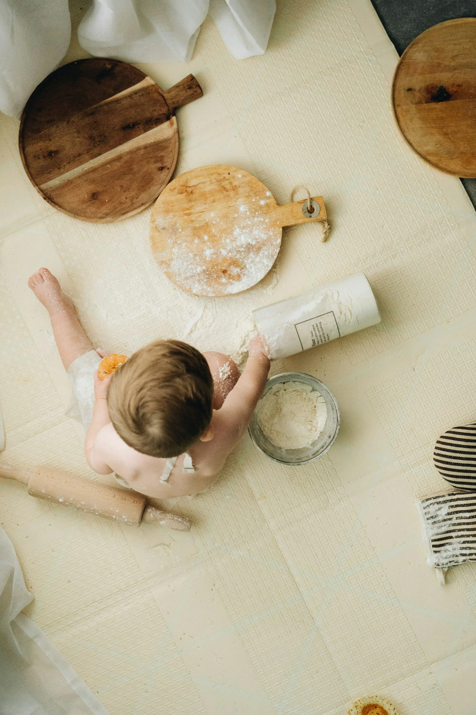 Child baking with flour on a light-colored table, surrounded by wooden cutting boards and baking tools.