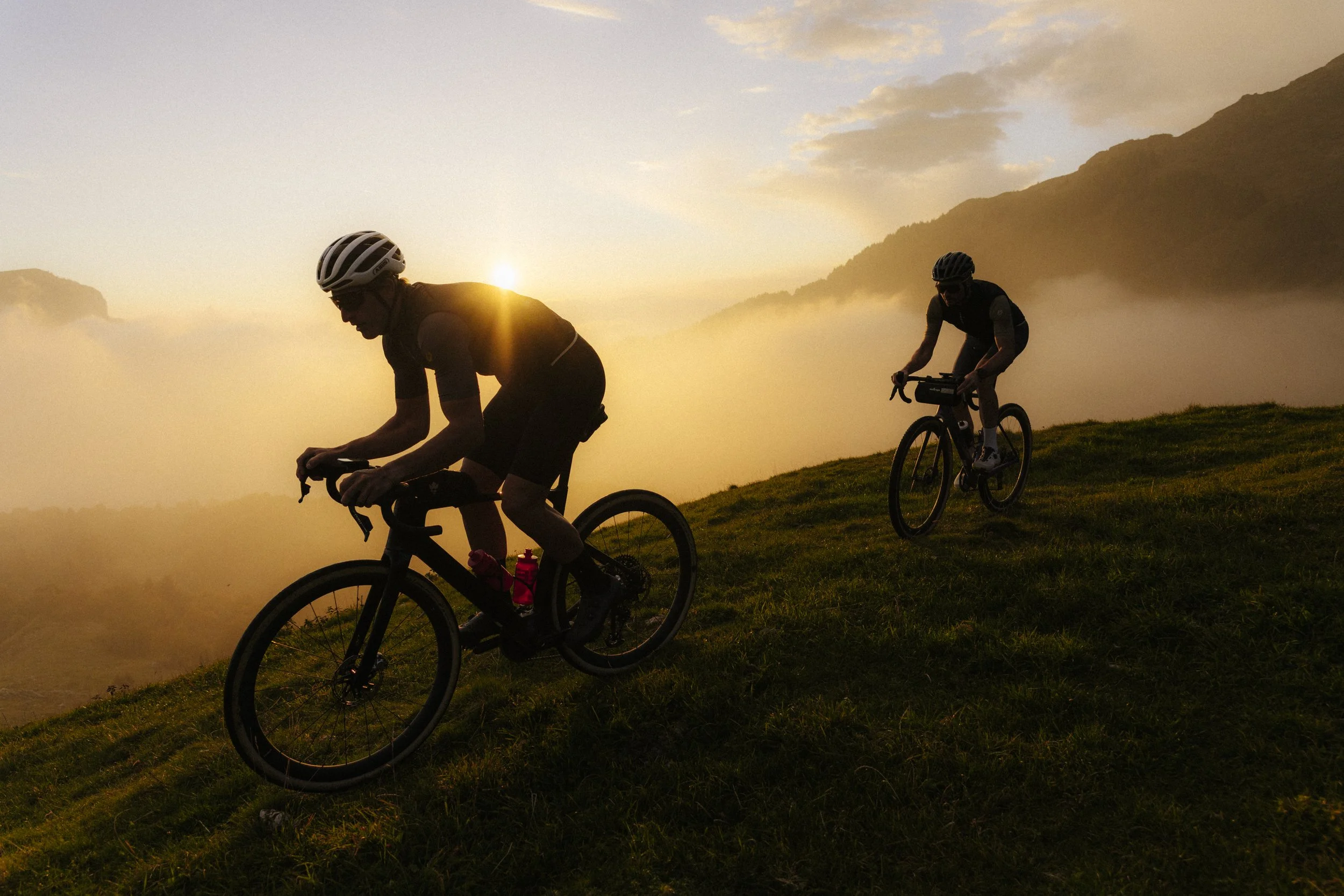 Deux cyclistes parcourent un chemin herbeux devant un soleil couchant