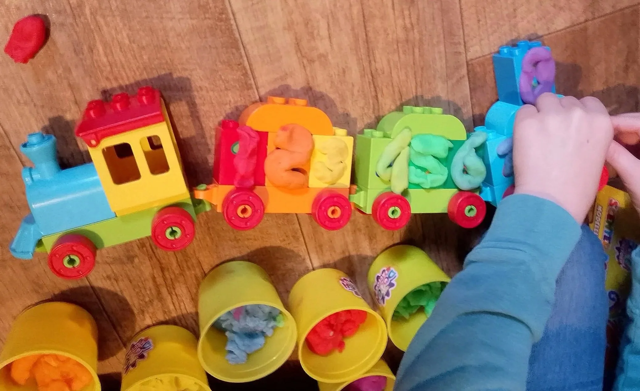 Child playing with colorful building blocks and toy buckets on a wooden floor.