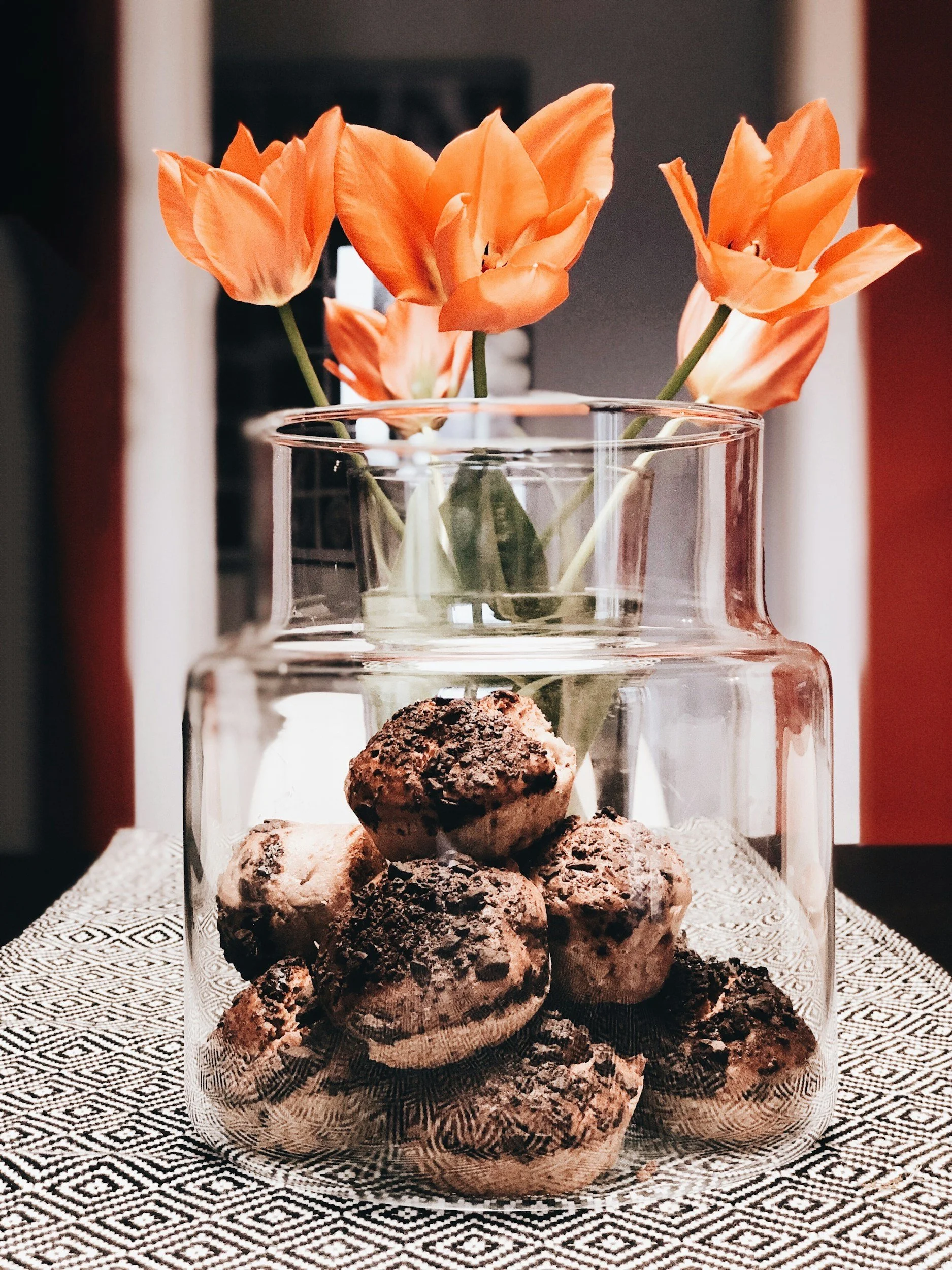 A glass vase holding orange flowers and a collection of chocolate chip cookies inside a glass jar.