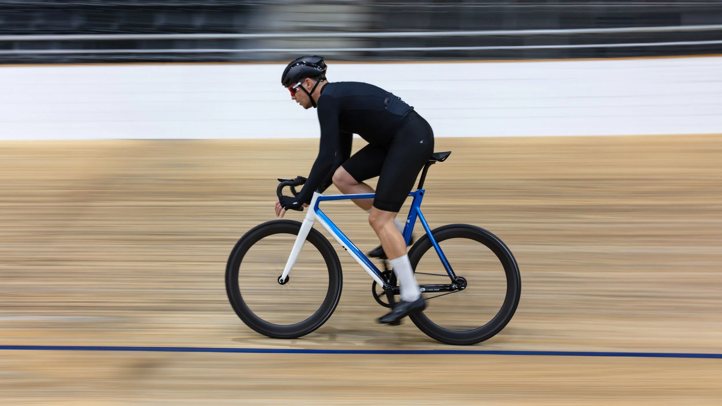 Un homme en tenue de cyclisme sur un vélo de track sur un piste en bois.