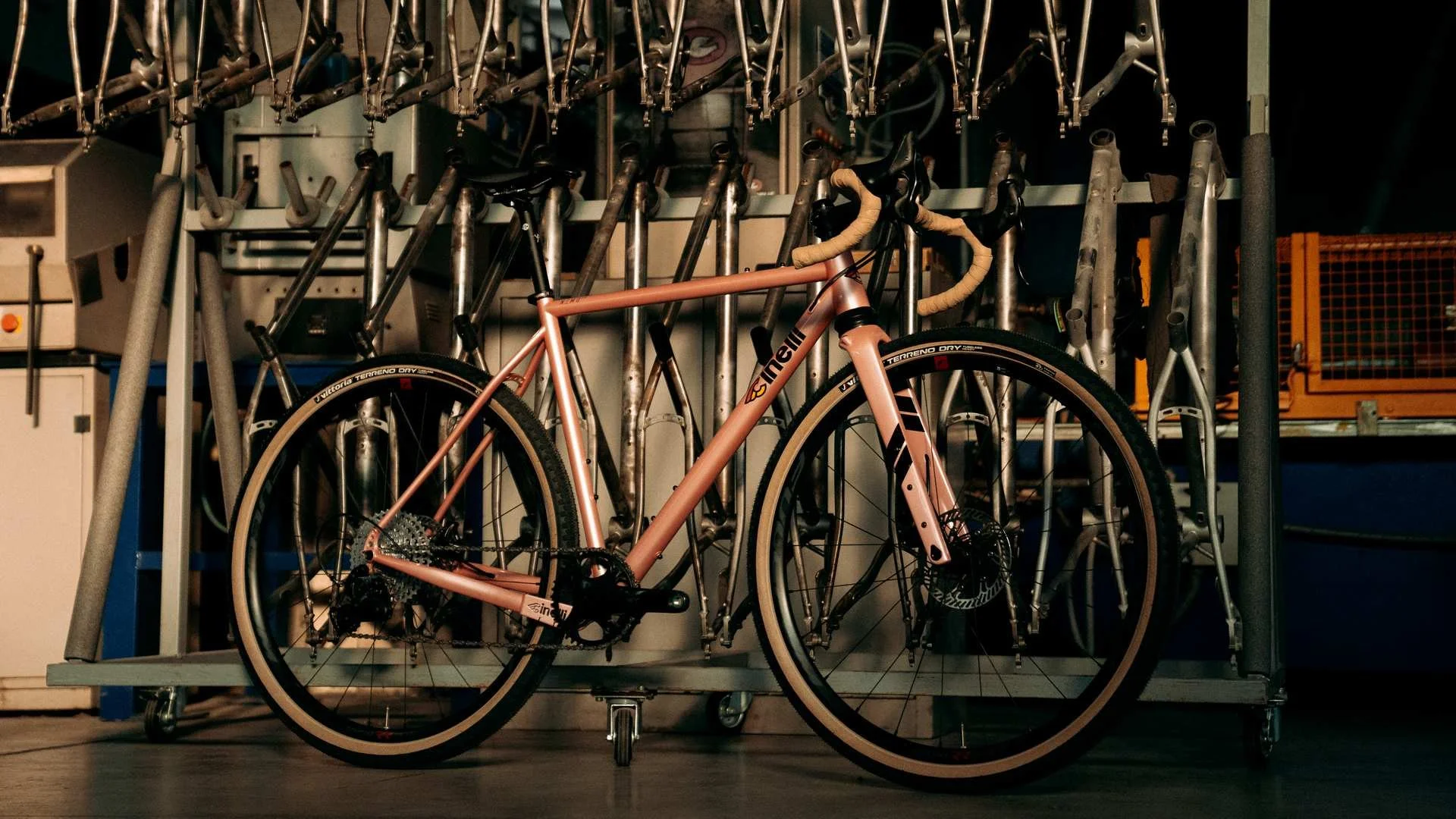 Vélo de couleur rose posé contre un support à vélos contenant plusieurs autres vélos ou cadres de vélo suspendus.