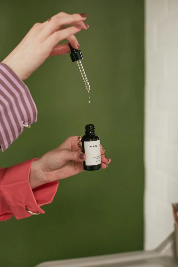 Two hands hold a small black bottle with a dropper, dispensing a liquid drop into the bottle.