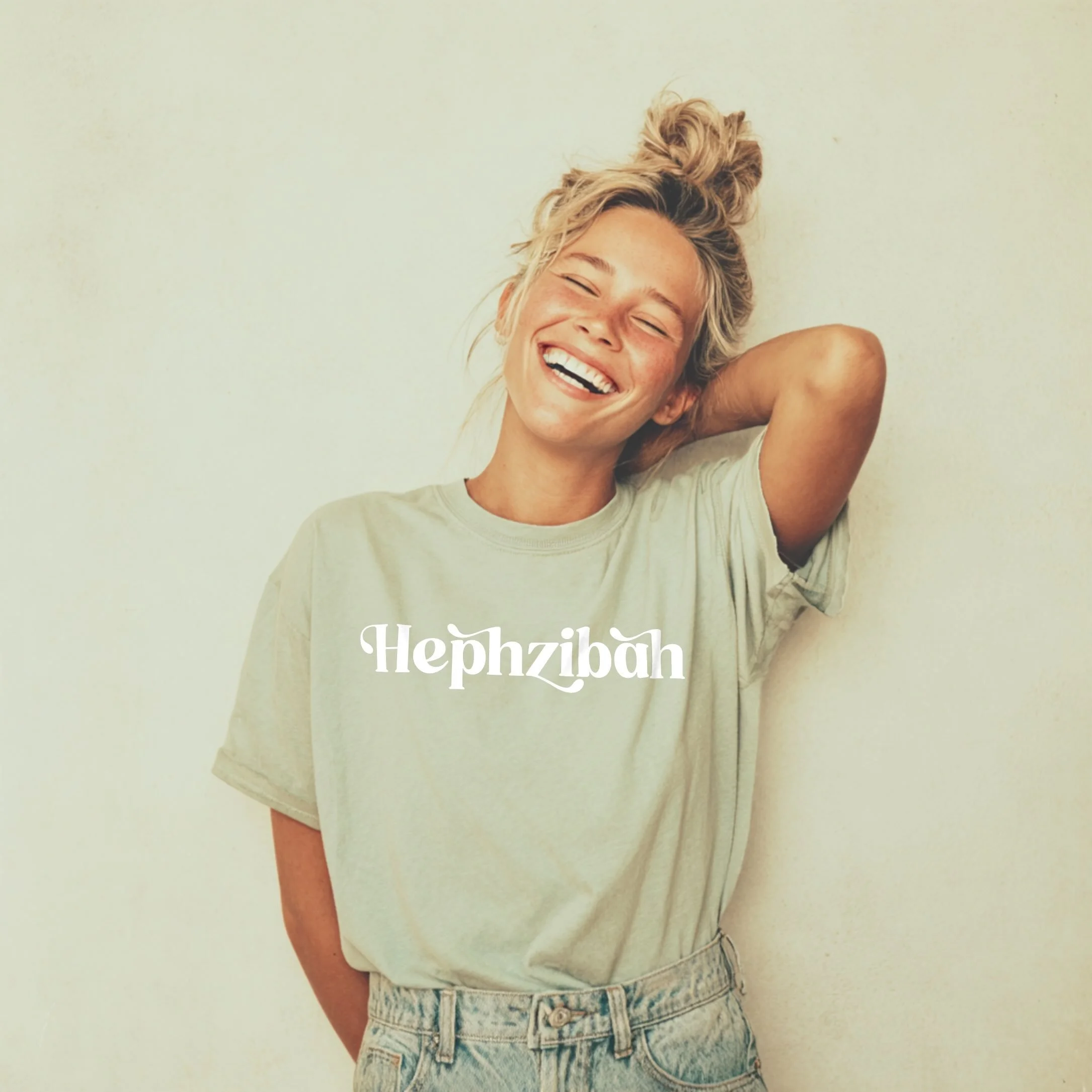 A blonde model wearing a Christian T-shirt in Army Green colour, with the word 'Hephzibah' written on the front in white