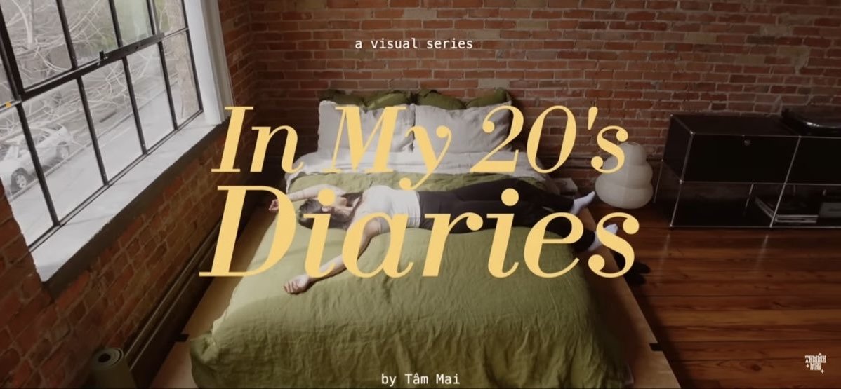 Ein Schlafzimmer mit rotem Ziegelstein an der Wand, einem großen Fenster, einem Bett mit grüner Decke und mehreren Kissen, auf dem eine Person liegt, die ein Buch liest.