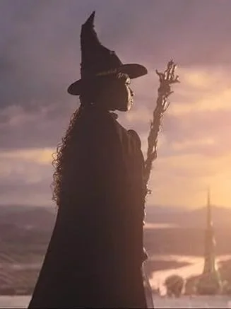 Eine Hexe in einem schwarzen Umhang und Hut bei Sonnenuntergang, die einen Zauberstab hält.