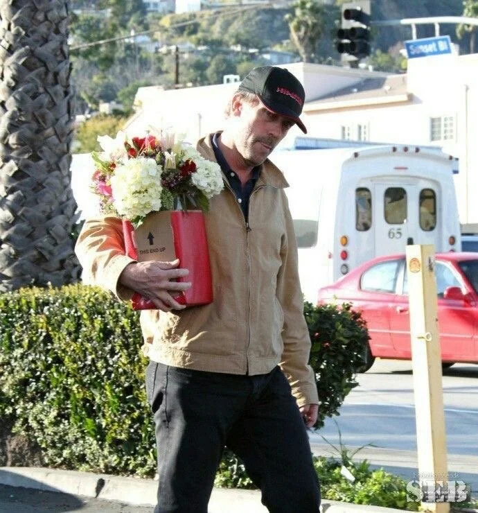 Actor Hugh Laurie Mann trägt einen Blumenstrauß in einer roten Schachtel an einer Straßenecke.